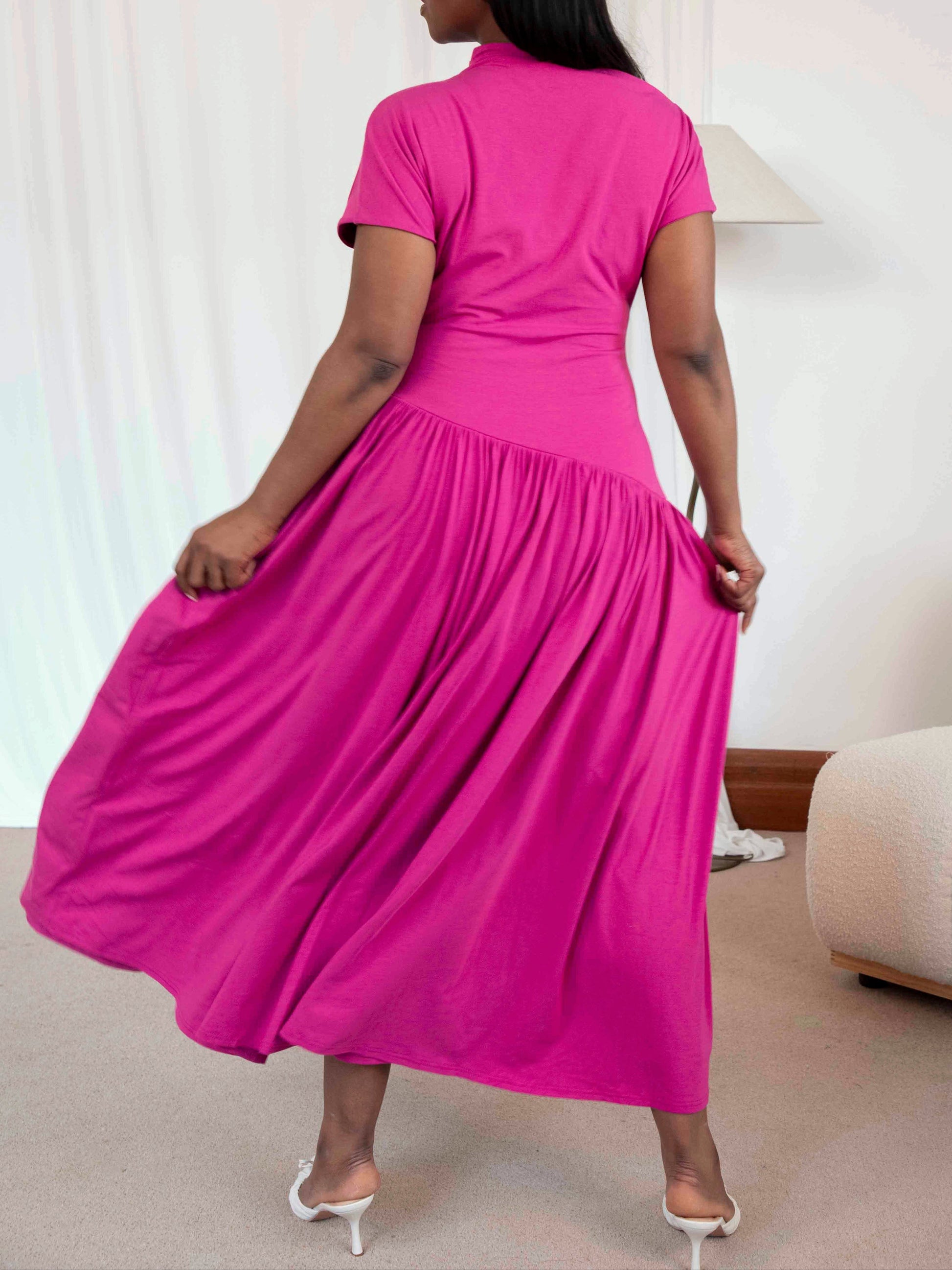Woman wearing a bright pink dress in a room with a white wall and beige sofa.
